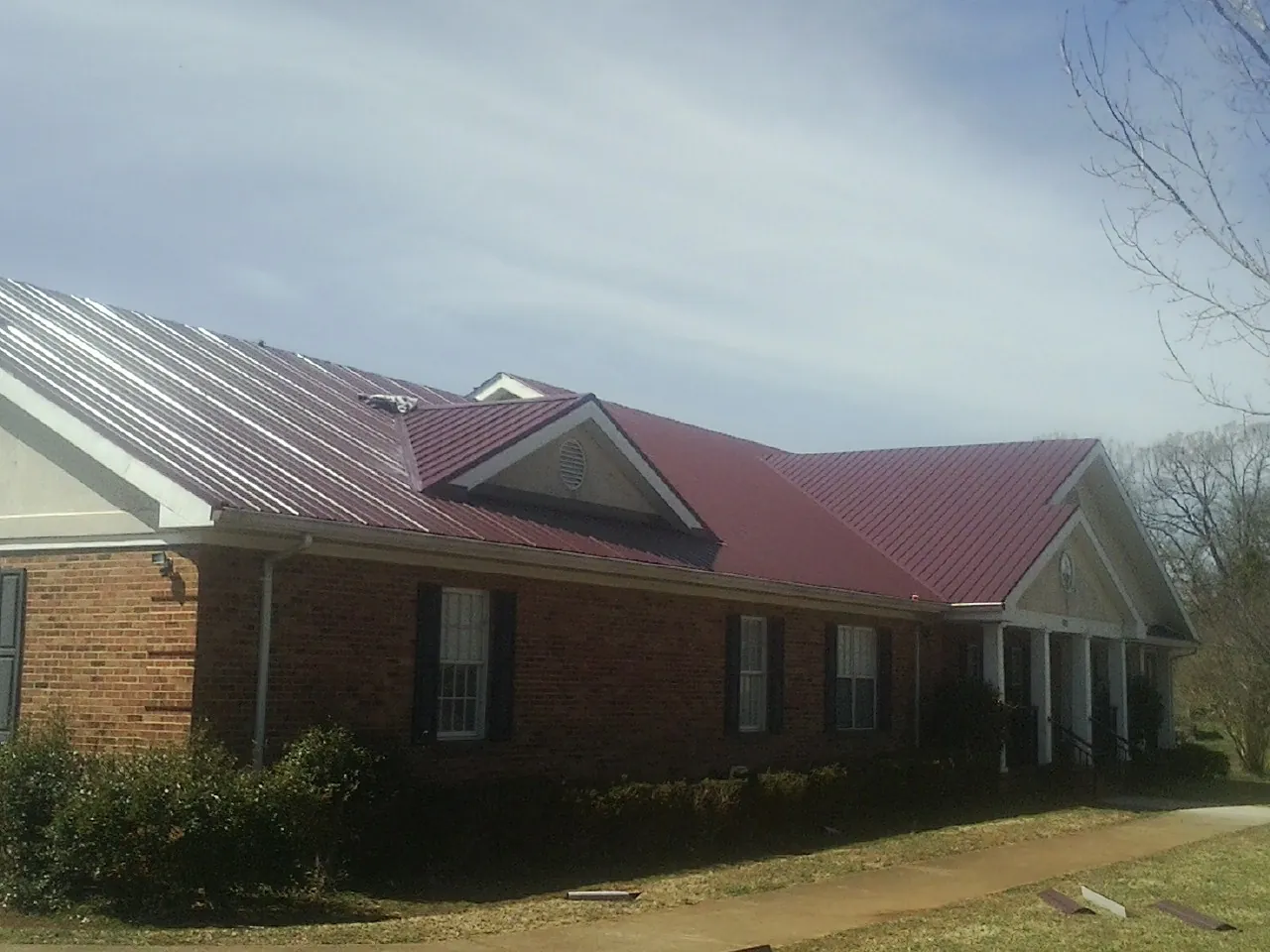 Red metal roof with gabled entries on a long brick building, from a Hail Damage Roof Repair job in Dothan