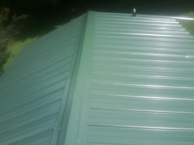 New green metal panels meeting at the ridge of a roof — Flat Roof Repair work by our crew in Dothan